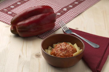 penne alla crema di peperone rosso e parmigiano su tavola in abete con forchetta e tovagliolo rosso.