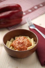 penne alla crema di peperone rosso e parmigiano su tavola in abete con forchetta e tovagliolo rosso.