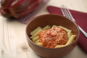 penne alla crema di peperone rosso e parmigiano su tavola in abete con forchetta e tovagliolo rosso.