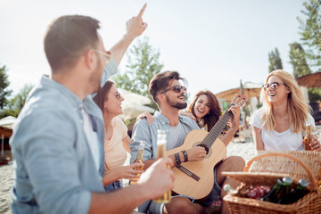 Group of friends with guitar and beer hanging out at beach