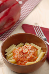 penne alla crema di peperone rosso e parmigiano su tavola in abete con forchetta e tovagliolo rosso.