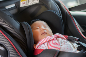 Asian women Mother takes care about her daughter in a car, helps her child fasten little young baby with car seat safety belt for infant,parent is keeping safe when riding in a vehicle on road.