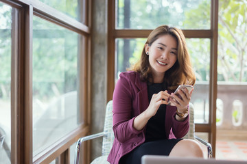 Smiling Business woman working in office with documents,Happy Asian businesswoman using phone sitting on chair at modern home studio.Concept of young people working mobile devices,contact to costumer