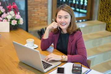 Asian woman working with laptop in coffee shop cafe,she smiling and holding pen