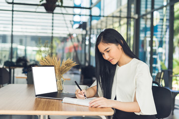 Fototapeta premium Young business woman reading a report her hand holding a pen sitting in a coffee shop and working on blank screen laptop.