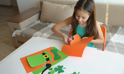 The girl cuts out a mask from paper for a St. Patrick's Day