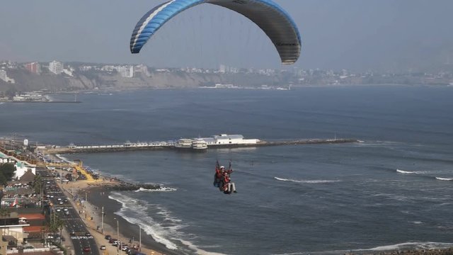 paraglider with a blue canopy flies at miraflores in lima, peru