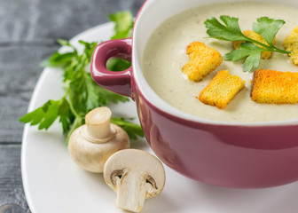 Cream soup of mushrooms with croutons in a purple bowl on a dark wooden table.