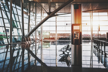 Modern pay phone station with screen mockup inside of interior of contemporary airport terminal with waiting hall, numerous seats, multiple steel beams, reflective floor, and huge glass facade behind