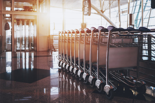 Close-up view row of multiple connected luggage carts stretching into distance parked in modern hall of airport terminal or railway depot station with elevator and glass facade in defocused background