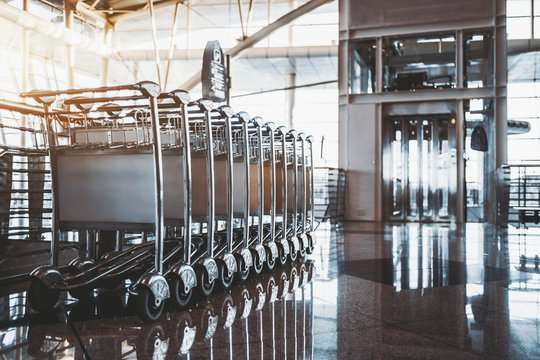 Row of multiple parked luggage carts in of contemporary bright airport terminal or railway station interior with reflective marble floor and chrome and glass elevator in a distance