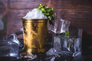 A container with ice stands among ice cubes and mint. - obrazy, fototapety, plakaty