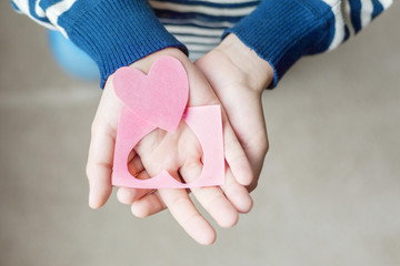 Pink heart in the palms. Close-up. Congratulations on Valentine's Day, Mother's Day, International Women's Day, Father's Day. Striped sweater.