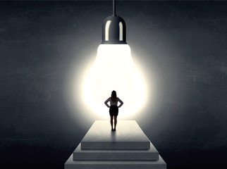 woman standing on a step in front of a huge light bulb