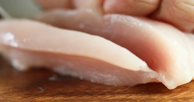  Close up the human hand cutting raw chicken meat on wooden chop board in kitchen room , 4K Dci resolution