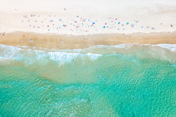 People swimming at the beach in summer with blue water from an aerial perspective