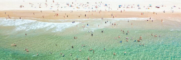 People swimming at the beach in summer with blue water from an aerial perspective