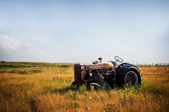 An old vintage red rusted tractor sitting in a fenced pasture in an agricultural rural summer countryside landscape