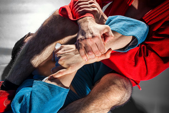 Close-up two wrestlers of sambo and jiu jitsu in a blue and red kimono doing . Man wrestler makes submission wrestling or armbar on gray tatami