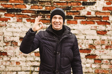 Obraz premium the guy smiles and shows the gesture okay. portrait. Brick wall