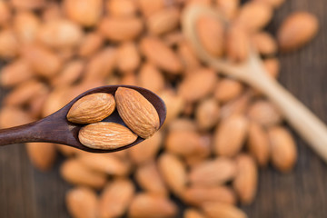 Top view of raw almonds nut on wood spoon and blurred group of almonds on a background.