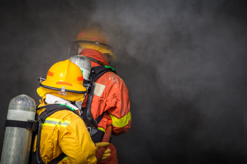 Obraz premium dwóch strażaków rozpryskuje wodę za pomocą dyszy wysokociśnieniowej, aby wypalić otoczenie dymem