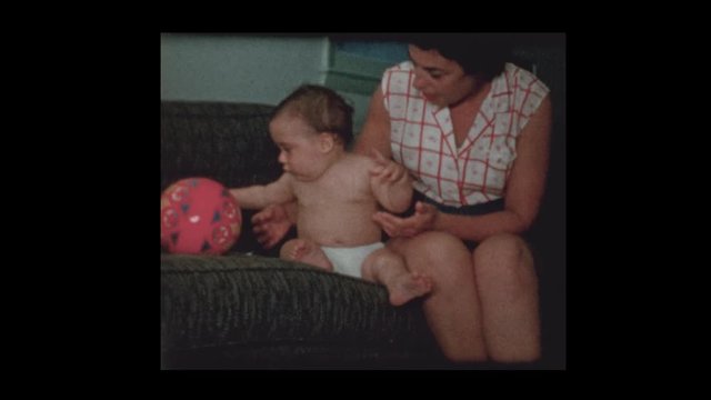 1960 Mother give infant baby boy in diapers a coaster to play with