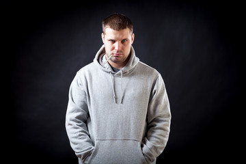 Fototapeta premium A young, dark-haired, sad-looking man in a sporty gray sweatshirt fell ill with a cold, measured the temperature on a black isolated background. A man holding a thermometer in his mouth
