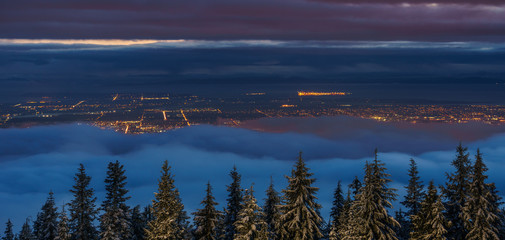 City view from top of the mountain in winter over the clouds at night.