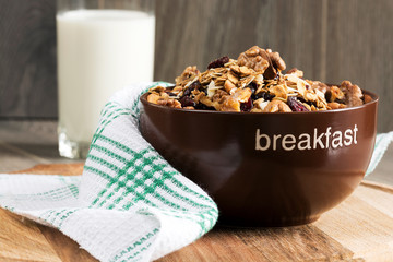 Homemade granola with honey, oatmeal, cashew nut, almond, pistachio, raisin and cranberry in clay bowl, glass with milk on wood dark table,