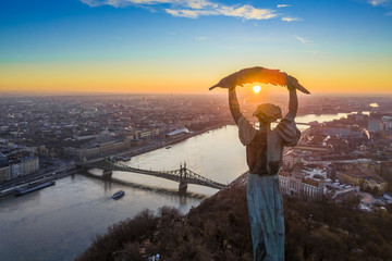 Budapest, Hungary - Aerial panoramic sunrise view at the Statue of Liberty with Liberty Bridge and sightseeing boat on River Danube taken from Gellert Hill - obrazy, fototapety, plakaty