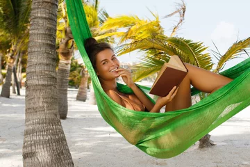 Poster Happy and beautiful woman lying in the hammock and reading book © blackday
