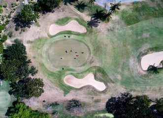Aerial view over golfers on the green near sand traps enjoying a fall game