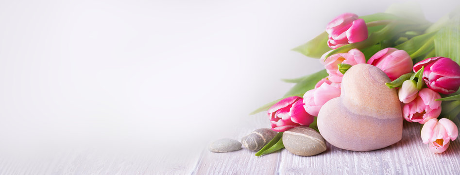 Beautiful tulips with stone heart on light wooden background