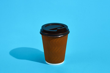 Hot coffee in brown paper cup with black lid on blue background 