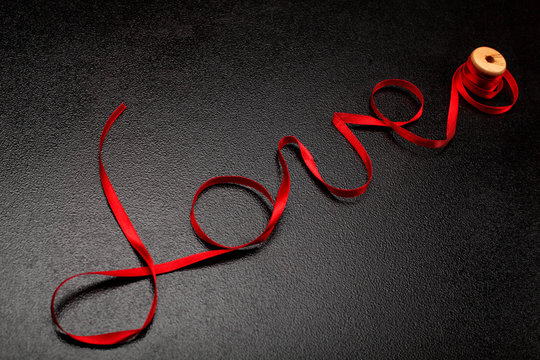 Inscription, word love of red satin ribbon.Valentine day background.Love concept.On dark stone background..Creative