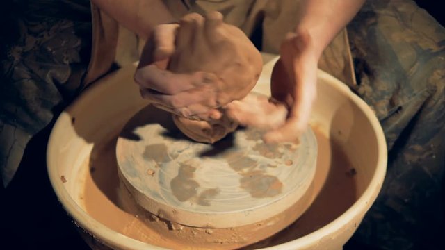 Potters hands shape clay lumps over a wheel. 