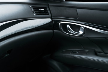 Obraz na płótnie Canvas Car black perforated leather interior details of door handle with windows controls and adjustments. Car door handle inside the luxury modern car. Switch button control