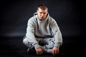 A young sad man in sports clothes got sick with the flu and does not know how he is treated, put a thermometer in his mouth to measure temperature on a black isolated background.