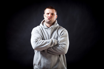 A young, dark-haired, sad man in a sporty gray sweatshirt fell ill with a cold, measures the temperature and makes grimaces on a black isolated background.