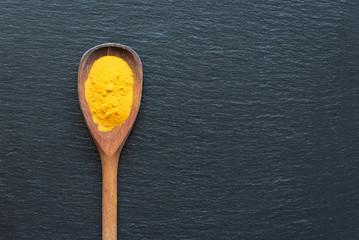 Turmeric powder in wooden spoon over black stone background, top view with copy space