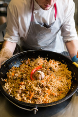 Chef cooking plov in the kitchen. Traditional famous Uzbek rice meal.