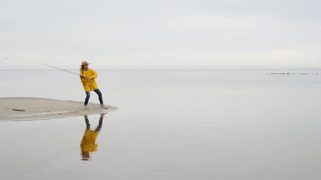 Fisherman in yellow raincoat throws fishing tackles with spinning rod in slow motion.