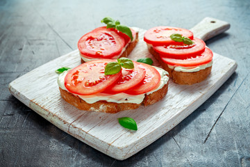 Bruschetta, toast with soft cheese, basil and tomatoes on a white wooden board. Italian healthy snack, food.