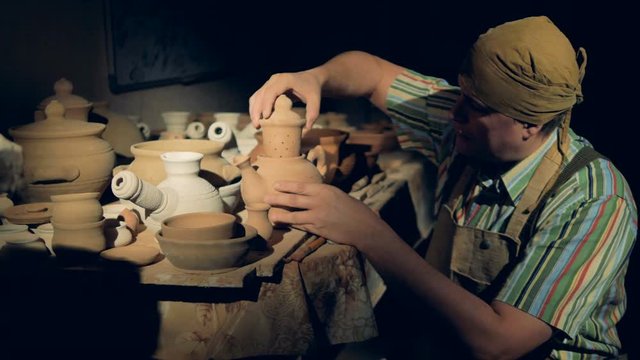 A potter inserts a clay tea strainer into a teapot. 