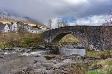 Fototapeta na wymiar Stone Bridge of Orchy in Scotland against a cloudy sky with house in the background