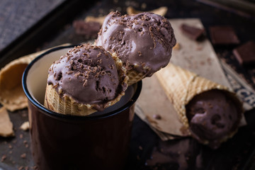 Homemade chocolate ice cream in waffle cones and pieces of dark chocolate on a dark metal tray on wooden table background, rustic. Copy space, top view