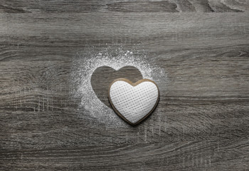 on a wooden background with powdered powder snow a silhouette of the heart is poured and below on the silhouette lies a cookie in the form of a heart 