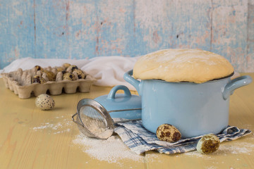 A special yeast dough for making homemade pies and buns in a small saucepan, next to quail eggs and a sieve for sifting the flour. 