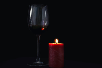 Burning candle and glass of wine on black background